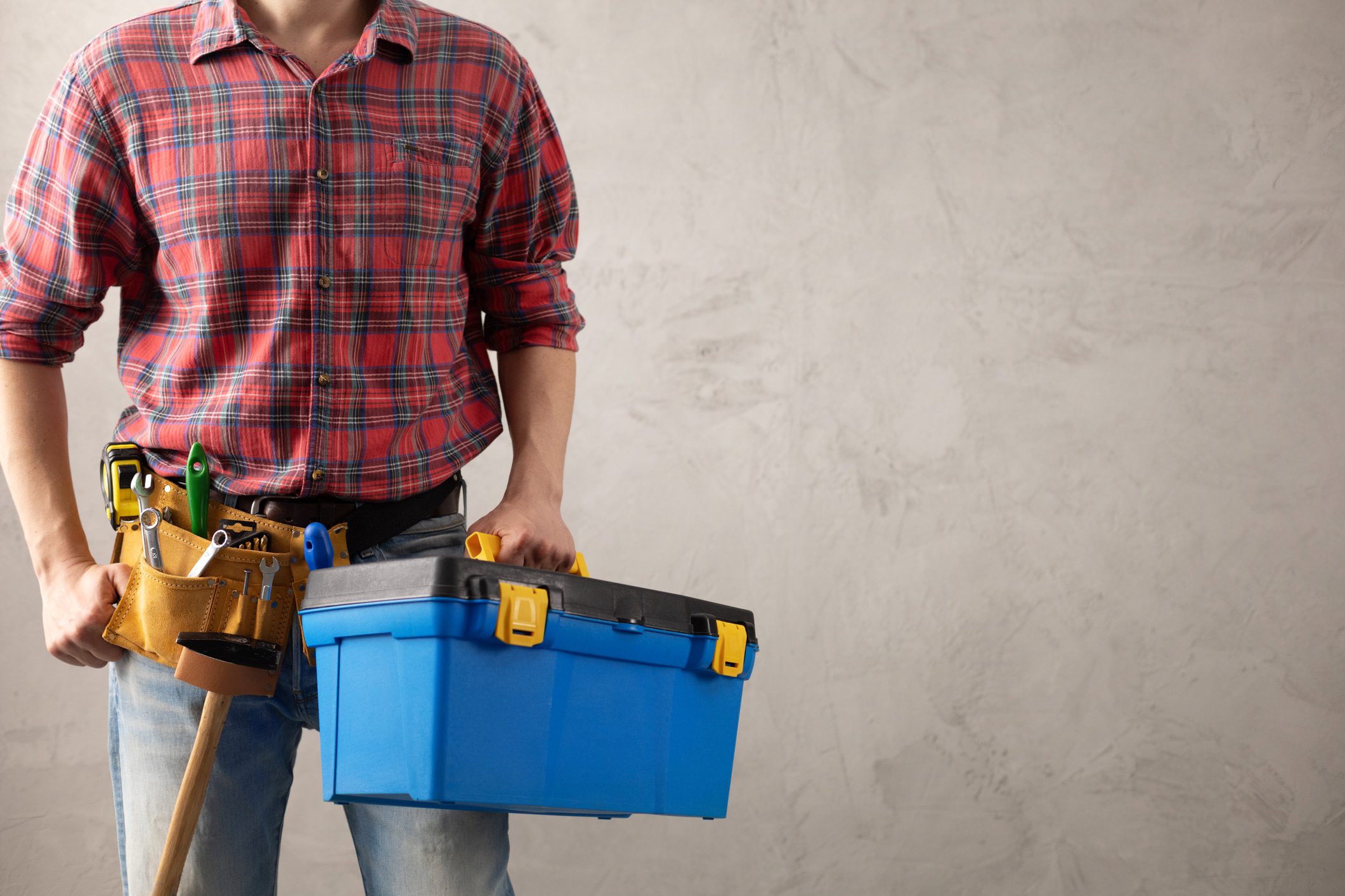 Man worker holding toolbox and tool belt near wall